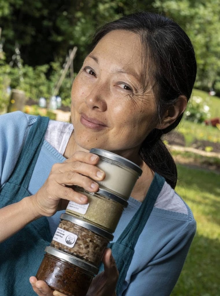 A woman holding a stack of jars of food.