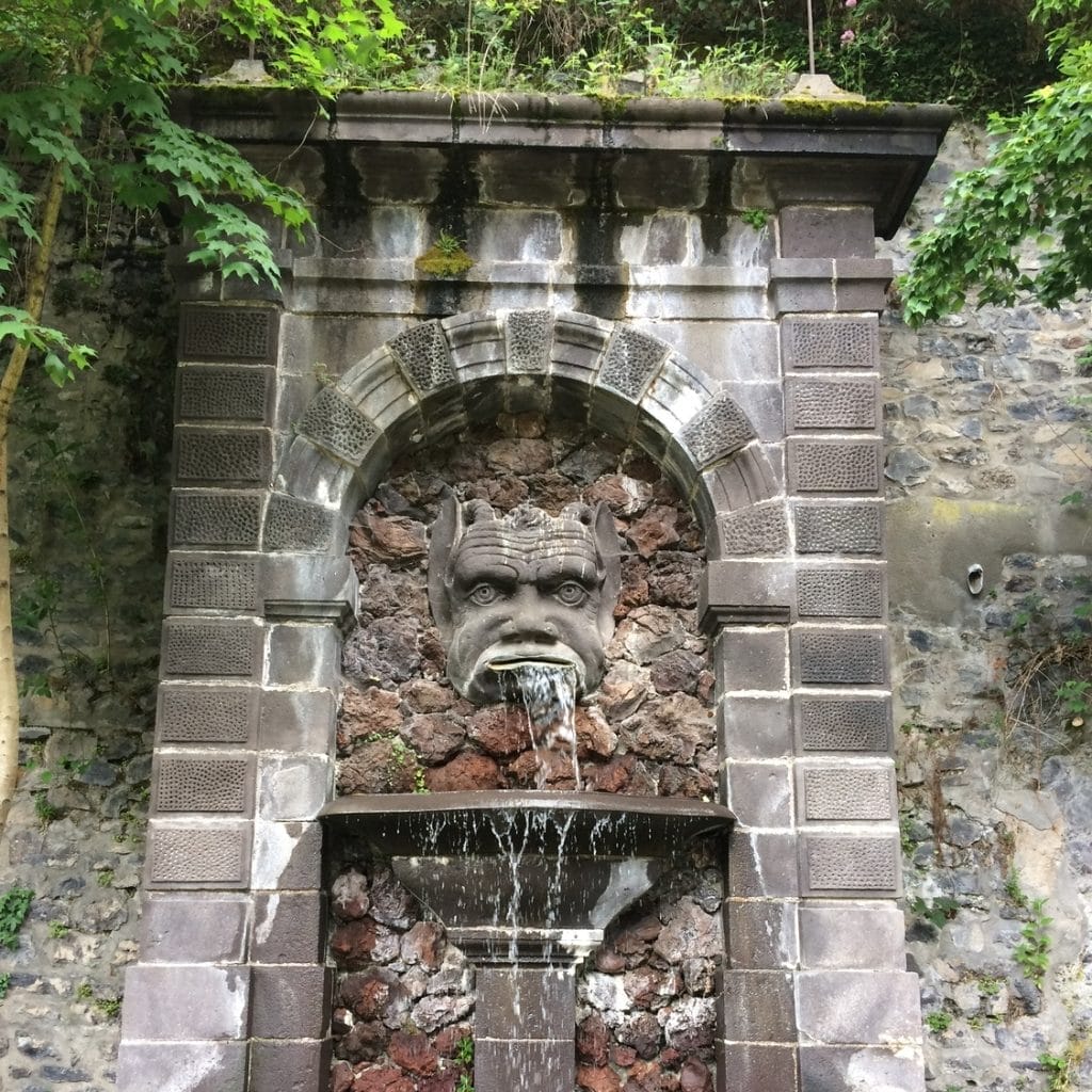 A fountain in a stone wall with a face on it.